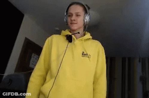 A Young Woman Wearing A Yellow Hoodie And Headphones Is Standing In A Room . GIF