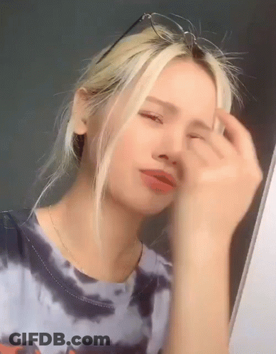 A Young Woman Wearing Glasses And A Tie Dye Shirt Is Looking At Herself In The Mirror . GIF