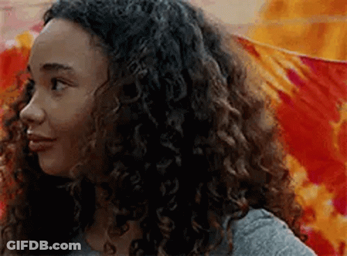 A Young Woman With Curly Hair Is Standing In Front Of A Colorful Wall . GIF
