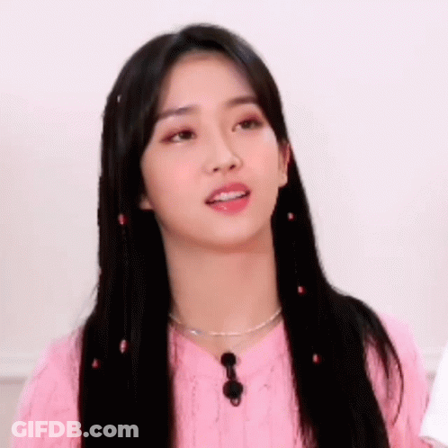 A Young Woman With Long Black Hair Is Wearing A Pink Sweater And Necklace . GIF