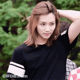A Young Woman With Long Blonde Hair Is Wearing A Black Shirt And Holding Her Hair . GIF