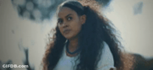 A Young Woman With Long Curly Hair Is Standing In Front Of A Smokey Background . GIF
