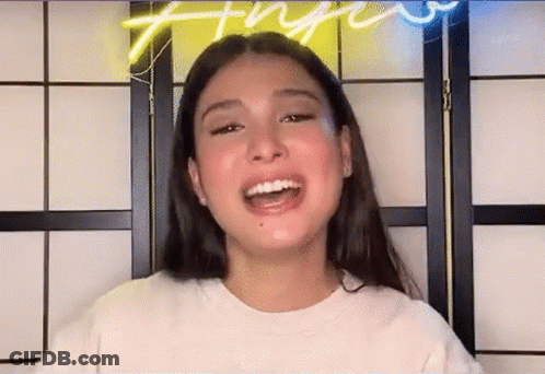 A Young Woman With Long Hair Is Smiling In Front Of A Neon Sign . GIF