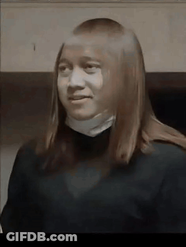 A Young Woman With Long Hair Is Wearing A Black Sweater And A White Collar . GIF