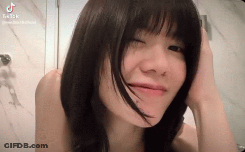 A Young Woman With Short Black Hair Is Making A Funny Face While Holding Her Hair . GIF