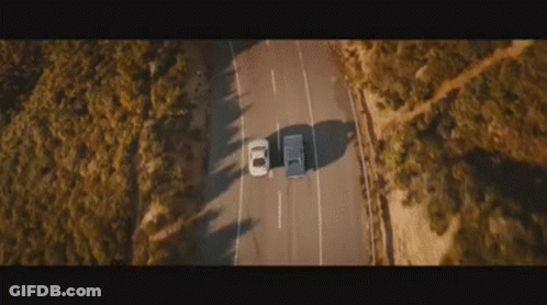 An Aerial View Of A Car Driving Down A Road . GIF