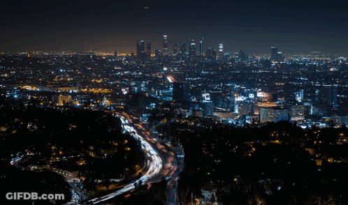 An Aerial View Of A City At Night With A Highway In The Foreground And The City Skyline In The Background GIF