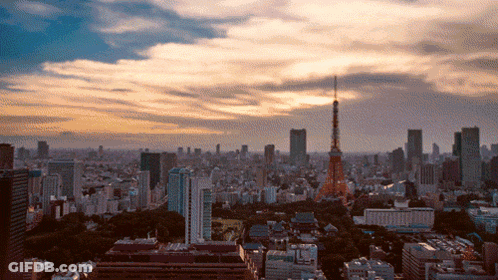 An Aerial View Of A City At Sunset With A Tower In The Foreground GIF