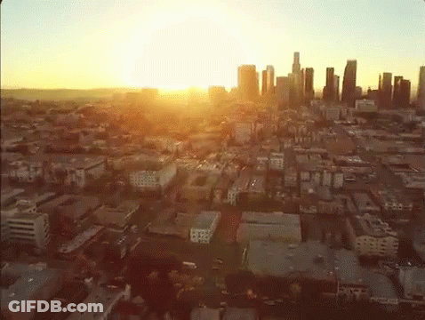 An Aerial View Of A City At Sunset With The Sun Shining Through The Clouds GIF
