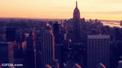 An Aerial View Of A City Skyline At Sunset With The Empire State Building In The Foreground GIF