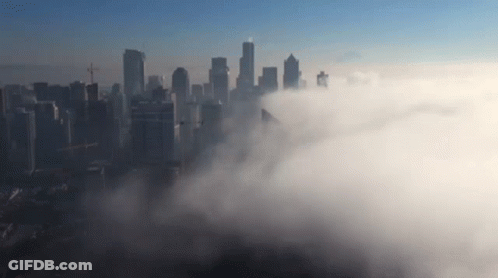 An Aerial View Of A City Skyline Covered In Clouds GIF