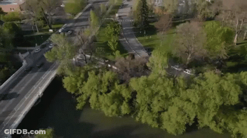 An Aerial View Of A City With A Bridge Over A River Surrounded By Trees . GIF