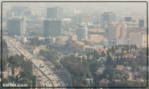 An Aerial View Of A City With A Highway In The Foreground And A Few Buildings In The Background GIF