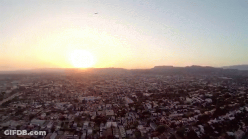 An Aerial View Of A City With The Sun Setting In The Background GIF