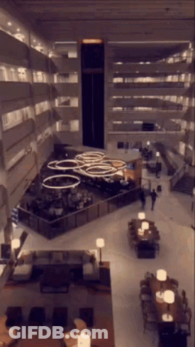 An Aerial View Of A Hotel Lobby With Tables Chairs And Stairs GIF