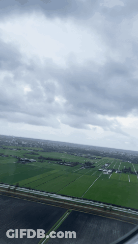 An Aerial View Of A Lush Green Field With A Cloudy Sky In The Background GIF