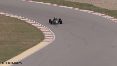 An Aerial View Of A Race Car On A Track With A Fence Behind It GIF