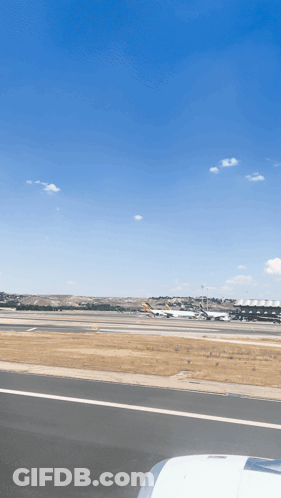 An Airport Runway With Planes Parked On It And A Blue Sky GIF