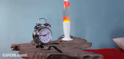 An Alarm Clock Sits On A Table Next To A Lava Lamp And A Watch GIF