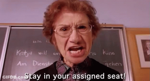 An Angry Teacher Says Stay In Your Assigned Seat In Front Of A Chalkboard GIF