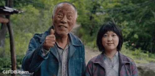An Elderly Man And A Young Girl Are Standing Next To Each Other . The Man Is Giving A Thumbs Up Sign . GIF