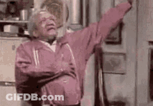 An Elderly Man In A Pink Jacket Is Dancing In A Kitchen With His Arms Outstretched . GIF