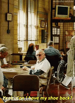 An Elderly Man In A Wheelchair Is Sitting At A Table In A Nursing Home And Asking If He Can Have His Shoe Back GIF