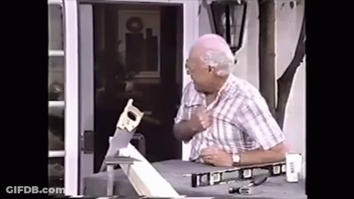 An Elderly Man Is Cutting A Piece Of Wood With A Saw On A Table . GIF