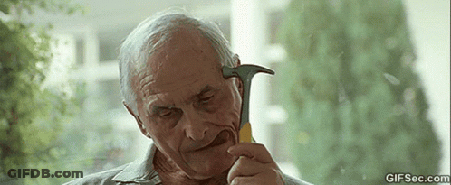 An Elderly Man Is Holding A Hammer In His Mouth And Looking At It . GIF