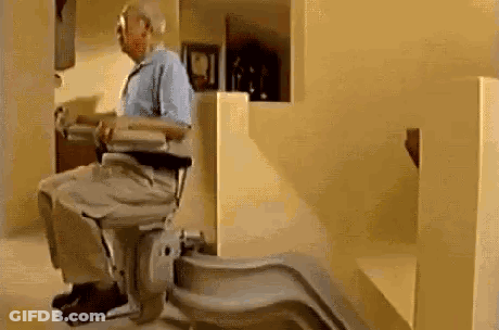 An Elderly Man Is Sitting On A Stair Lift In A House . GIF