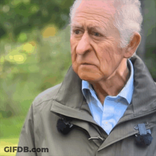 An Elderly Man Wearing A Grey Jacket And Blue Shirt GIF