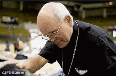 An Elderly Man Wearing Glasses And A Black Shirt Is Talking To A Group Of People . GIF