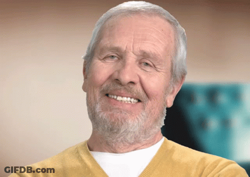 An Elderly Man With A Beard And Yellow Sweater Smiles GIF