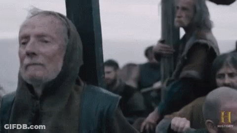 An Elderly Man With A Hood On His Head Is Sitting On A Boat With Other Men . GIF