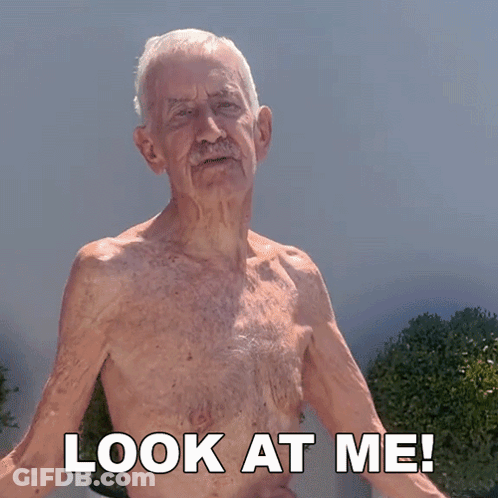 An Elderly Man Without A Shirt Is Standing In Front Of A Sign That Says Look At Me GIF