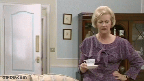 An Elderly Woman In A Purple Dress Is Holding A Cup Of Coffee In A Living Room . GIF