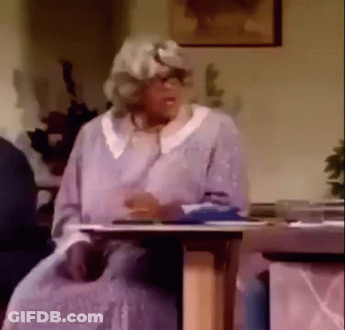 An Elderly Woman In A Wig Is Sitting At A Table . GIF