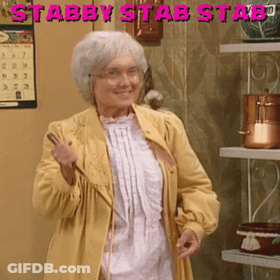 An Elderly Woman In A Yellow Coat Is Holding A Wand In Front Of A Sign That Says Stabby Stab Stabd GIF