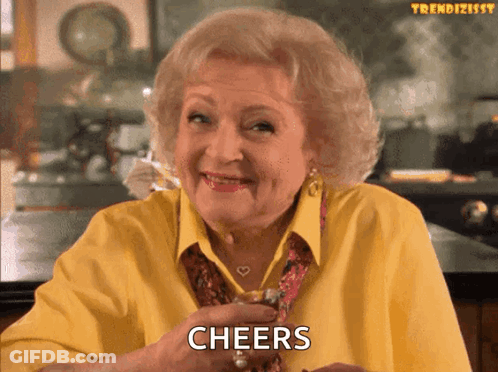 An Elderly Woman In A Yellow Shirt Is Holding A Glass Of Whiskey And Says Cheers GIF