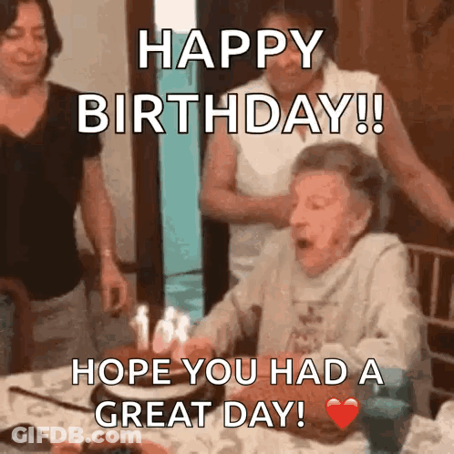 An Elderly Woman Is Blowing Out Candles On A Birthday Cake While Sitting At A Table . GIF