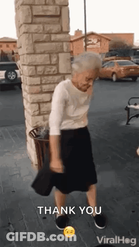 An Elderly Woman Is Dancing In Front Of A Brick Wall In A Parking Lot While Holding A Hat . GIF