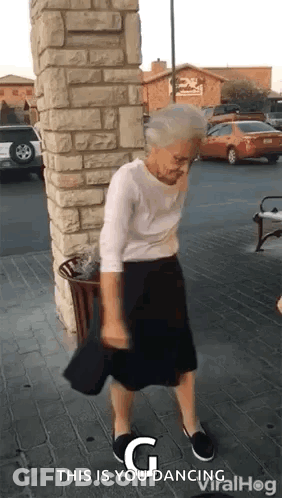 An Elderly Woman Is Dancing On The Sidewalk In Front Of A Brick Building . GIF