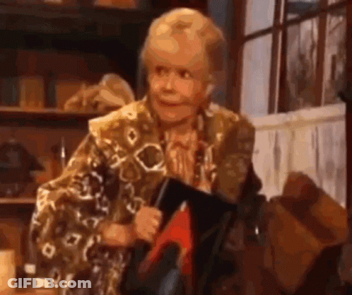 An Elderly Woman Is Holding A Book And Smiling While Sitting In Front Of A Window . GIF