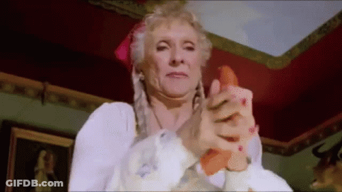 An Elderly Woman Is Holding A Carrot In Her Hand And Making A Funny Face . GIF