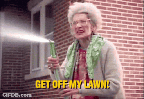 An Elderly Woman Is Holding A Hose In Front Of A Brick Building And Saying `` Get Off My Lawn '' . GIF