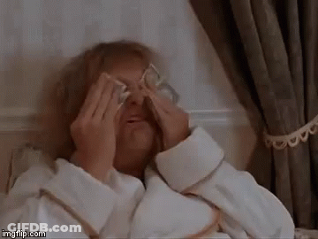 An Elderly Woman Is Laying In A Bed Covering Her Eyes With Money . GIF
