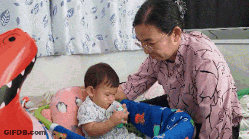 An Elderly Woman Is Playing With A Baby In A Playpen GIF