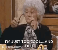 An Elderly Woman Is Sitting At A Table Holding A Pair Of Glasses . GIF