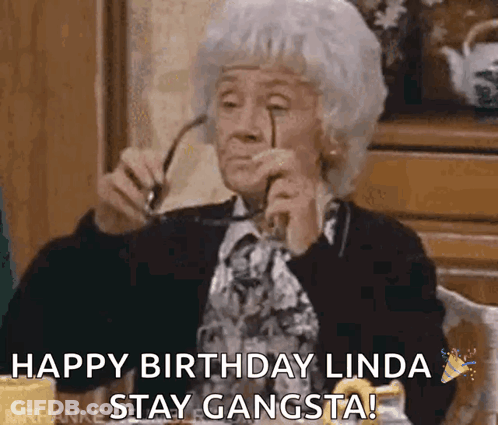 An Elderly Woman Is Sitting At A Table Holding Glasses And Saying Happy Birthday Linda Stay Gangsta ! GIF
