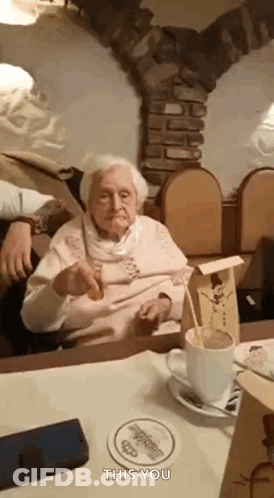 An Elderly Woman Is Sitting At A Table With A Cup Of Coffee And A Spoon . GIF